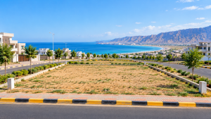 5B Marketing banner advertising a one-kanal residential plot in New Town Gwadar, featuring a vacant coastal plot, paved roads, modern homes, the Arabian Sea, and mountains.